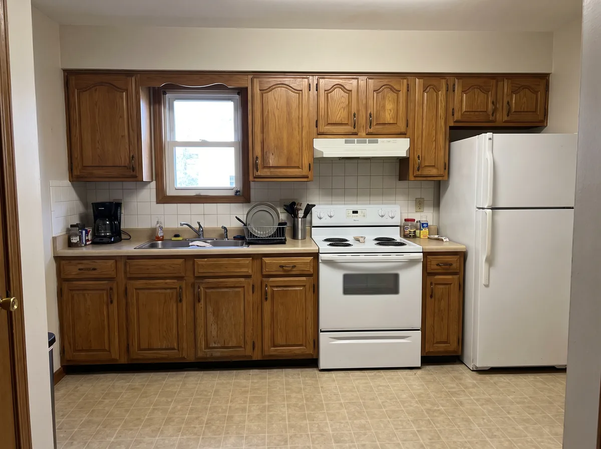 A dated kitchen with honey-oak cabinets, white appliances and a window over the sink — a generated demonstration room