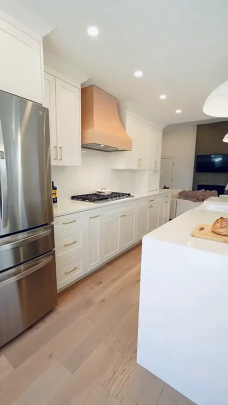 A white kitchen in daylight: a long island, a tall fridge run and a pendant over the counter