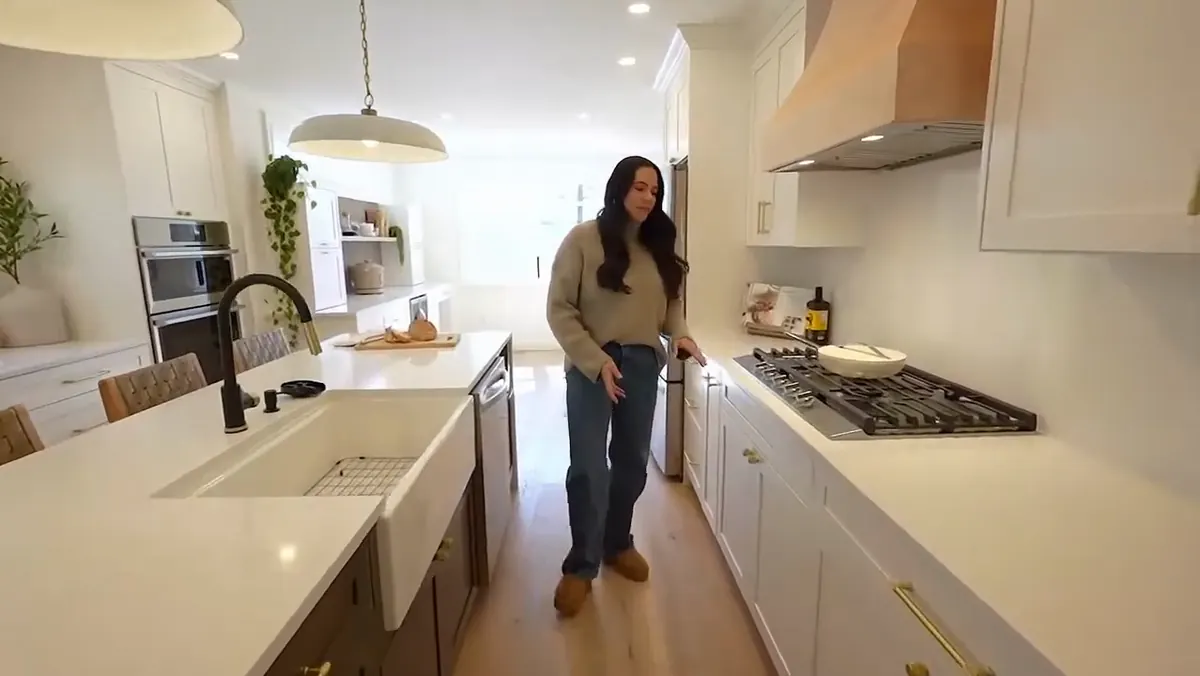 Brena Crow in the white kitchen she designed, the island on one side of her and the range run on the other