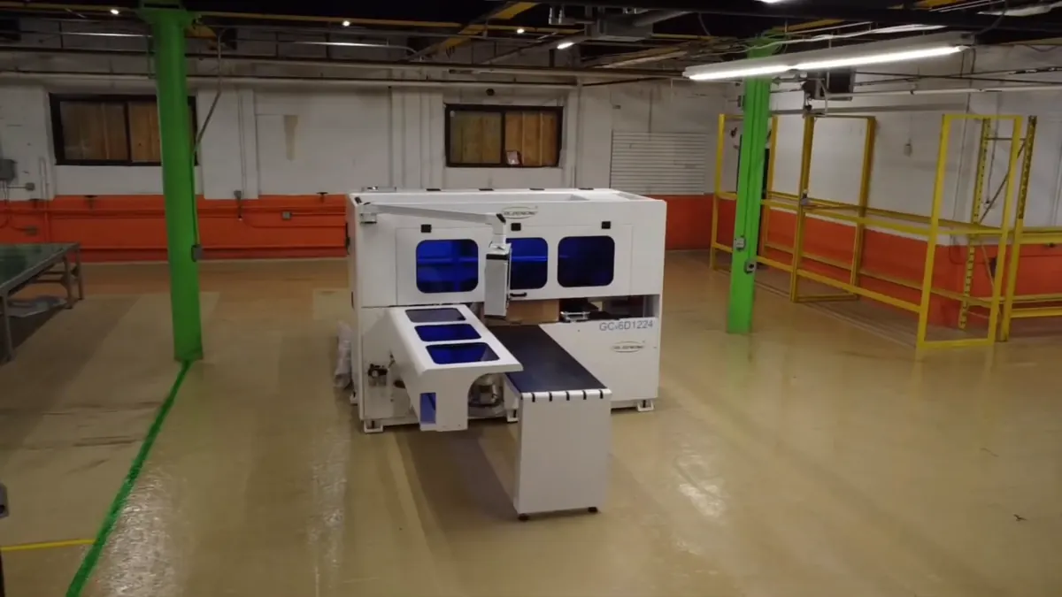 The production floor: a beam saw and edgebander under green steel columns, clear aisle down the middle