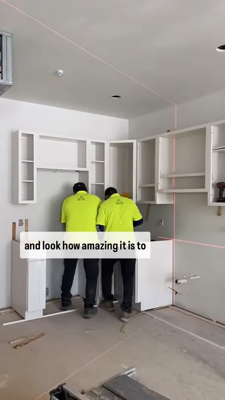Two installers in Quality Design Cabinet shirts hanging wall cabinets in an unfinished apartment