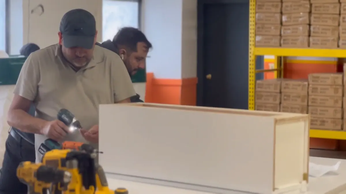 Two of the crew assembling a cabinet box at the bench, driver in hand