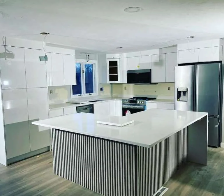 White gloss kitchen with a fluted island base, stainless fridge and black over-the-range microwave.