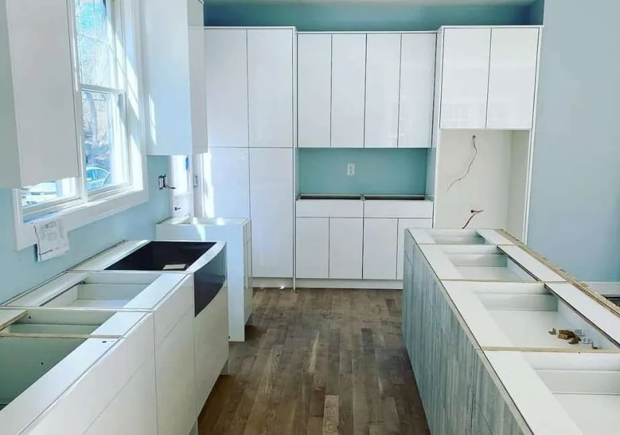 White flat-front kitchen going in against teal walls, sink base open