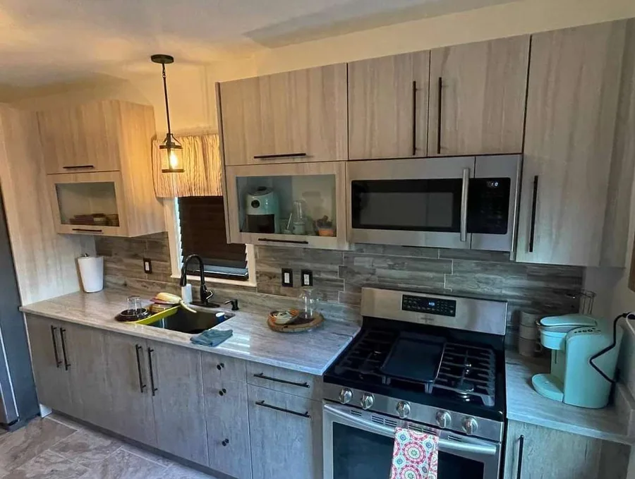Woodgrain flat galley run with stone backsplash, one glass-front upper cabinet, stainless gas range and over-the-range microwave and black bar pulls.