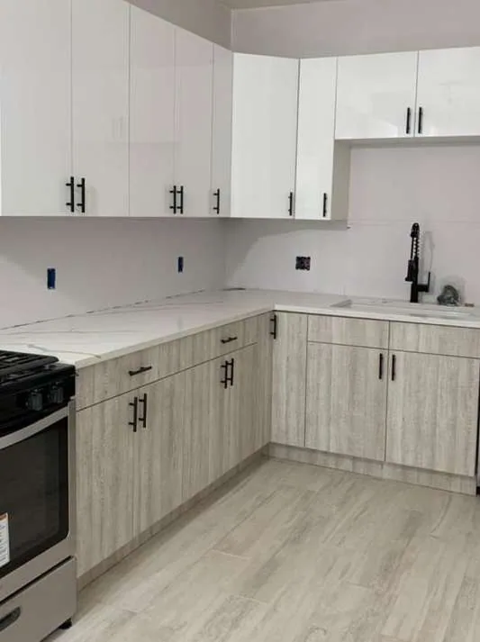 White gloss uppers over pale woodgrain lowers, L-run with matte black bar pulls, two-tone upper/lower split and gas range.